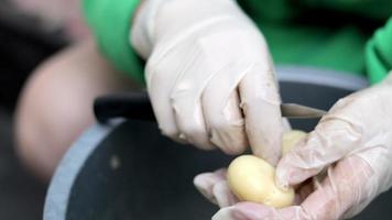 Woman's hands in white gloves peel raw new potatoes, close-up. Cleaning organic potatoes. Detail of female hands peeling fresh yellow potato with kitchen knife, food preparation concept. video