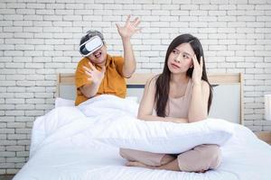 concept of family problems. An elderly Asian husband is very addicted to VR games. Makes the young wife bored that her husband is not interested in her. And sitting stressed out in bed in the bedroom. photo