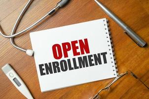 open enrollment, text on white notepad paper on wooden background near stethoscope photo