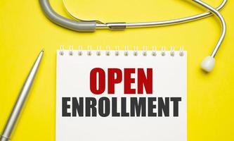 open enrollment, text on white notepad paper on yellow background near stethoscope photo
