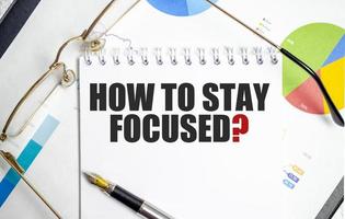 how to stay focused text written on white notebook with calculator and pen photo