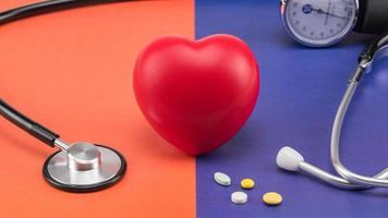 A heart-shaped antistress pulse sponge next to a phonendoscope and some pills on a two-colored background.