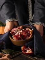 A vertical photo of woman's hands holding a bowl of pomegranate