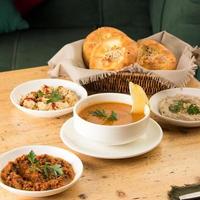 A closeup shot of a soup and appetizers near basket of breads