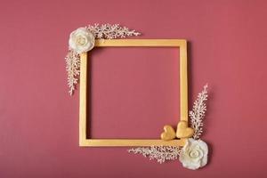 Square golden frame blank with roses and golden hearts on red background. Flat lay, top view, copy space photo
