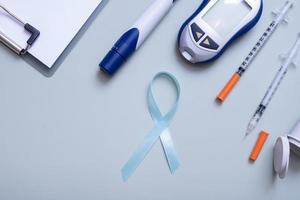 Blue ribbon and glucometer,  medical supplies on color background top view with copy space. World diabetes day concept photo