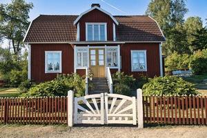 casa tradicional sueca roja y blanca en smalland, valla blanca jardín verde cielo azul foto