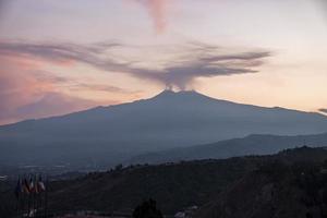 Smoke emitting from volcanic Mount Etna with luxurious Hotel Elios in foreground photo