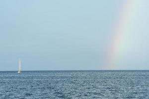 vista panorámica del arco iris en el cielo azul sobre el barco en el paisaje marino en un día soleado foto