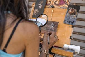 mujer pintando detalles en un pequeño lienzo fuera de la tienda en el mercado del casco antiguo foto