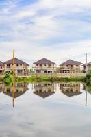 New house building reflection with water in lake at residential estate construction site with clouds and blue sky photo