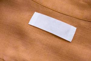 White blank clothing tag label on brown linen shirt fabric texture background photo