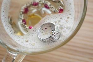 cleaning vintage jewelry diamond ring and bracelet in glass on wood table background photo