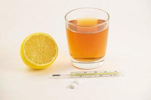 Hot tea with lemon, tablets and thermometer on white background. Healthy concept. Glass mercury thermometer with a high temperature. photo