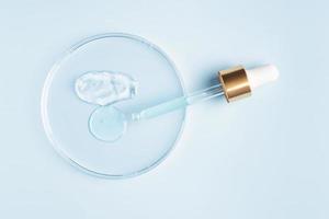 smear of cosmetic gel stroke and round transparent drop of serum in a petri dish on a blue background. Concept laboratory tests and research, making and testing cosmetic photo