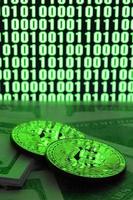 Two bitcoins lies on a pile of dollar bills on the background of a monitor depicting a binary code of bright green zeros and one units on a black background. Low key lighting photo