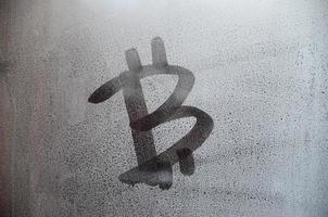 The bitcoin symbol on the misted sweaty glass. Abstract background image. Cryptocurrency concept photo