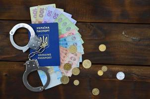 A photograph of a Ukrainian foreign passport, a certain amount of Ukrainian money and police handcuffs. The concept of arresting Ukrainian illegal immigrants while trying to bribe photo