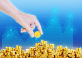 one hand is putting gold coins on pile of gold coins with graphic blue background photo