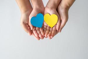 Save Ukraine Stop the war. Adult and child hands holding paper heart in the color of national flag of Ukraine.
