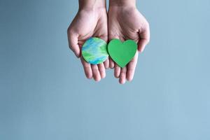 manos sosteniendo la tierra y forma de corazón verde. concepto de proteger al mundo del calentamiento global con eco-corazón en mente. foto