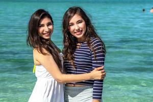 Two beautiful black hair girls smiling and playing on the beach photo