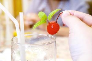 mano de mujer gorda está tomando una cereza roja del vaso para comer. foto