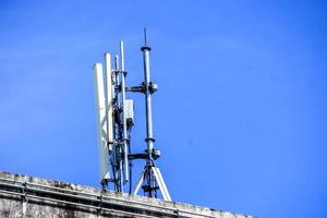 dispositivos y receptores de señal de comunicación con antenas en la parte superior del edificio y fondo de cielo azul brillante. foto