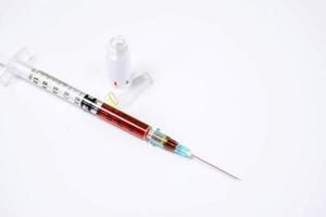 la ampolla de la droga se abre y la droga líquida se introduce en una jeringa de plástico con una aguja médica sobre fondo blanco. foto