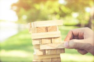 people hand playing take one brown wood block stack game on building tower. concept planning risk and strategy in and engineer construction. photo