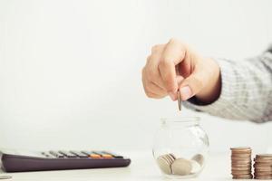 close up hand business man accounting calculate calculator expenses with savings money coins stacked row with hand putting coins Coins drop into piggy bank. concept Write Finance accounting. photo