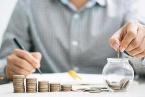 close up hand business man accounting calculator with savings money coins stacked row with hand putting coins in jug glass. concept Write Finance accounting. photo