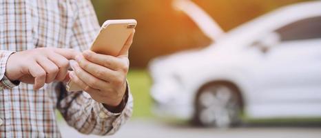 close up businessman hand using a mobile smart phone call a car mechanic ask for help assistance because car broken roadside. people journey friends standing wait beside broken car background. photo
