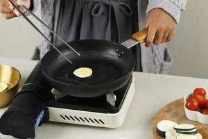 Cooking Hobak jeon, Korean Zucchini Pancake in the Kitchen, Put Sliced Zucchini with Egg Batter on Black Pan photo