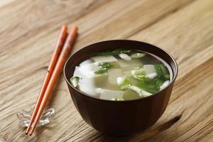 sopa de miso japonesa con cebolleta y tofu en cubos en un tazón marrón, mesa de madera. foto