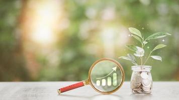 financial growth and investment ideas sustainable income and profit planning retirement preparation future fund management, magnifying glass Coin jar and tree all lay on the table photo