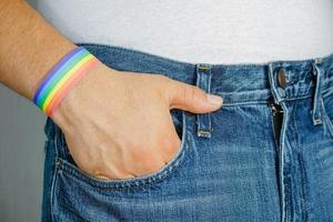 mano masculina con pulsera de arco iris usando jeans. concepto de libertad y lgbt foto