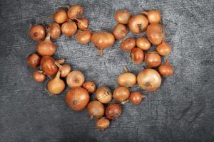 Many brown onions lie next to each other on a light gray background and form a heart photo