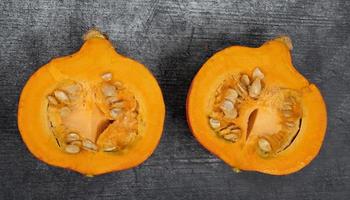 A bright orange Hokkaido pumpkin lies on a gray background. You can see the pulp and the seeds. photo