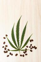 Coffee beans in a wooden spoon with cannabis leaves on a wooden table.copy space.flat lay.top-down.top view. photo