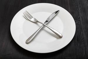 plato blanco con cuchillo cruzado, cuchara en la oscuridad foto