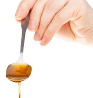 front view of hand holds metal spoon with honey photo