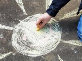 girl paints a sun with colored chalk on asphalt photo