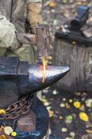 Blacksmith forges red glowing iron rod on anvil photo