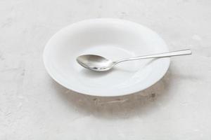 plato hondo blanco con cuchara de acero sobre hormigón gris foto