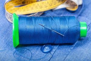 thread bobbin, button, measure tape on blue cloth photo