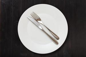 top view of white plate with flatware on dark photo