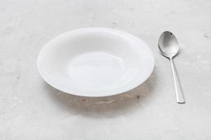 white deep plate and metal spoon on gray concrete photo