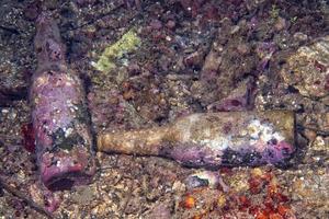 encrusted bottle on the sand bottom of the ocean photo