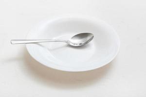 plato hondo blanco con cuchara de acero sobre yeso foto
